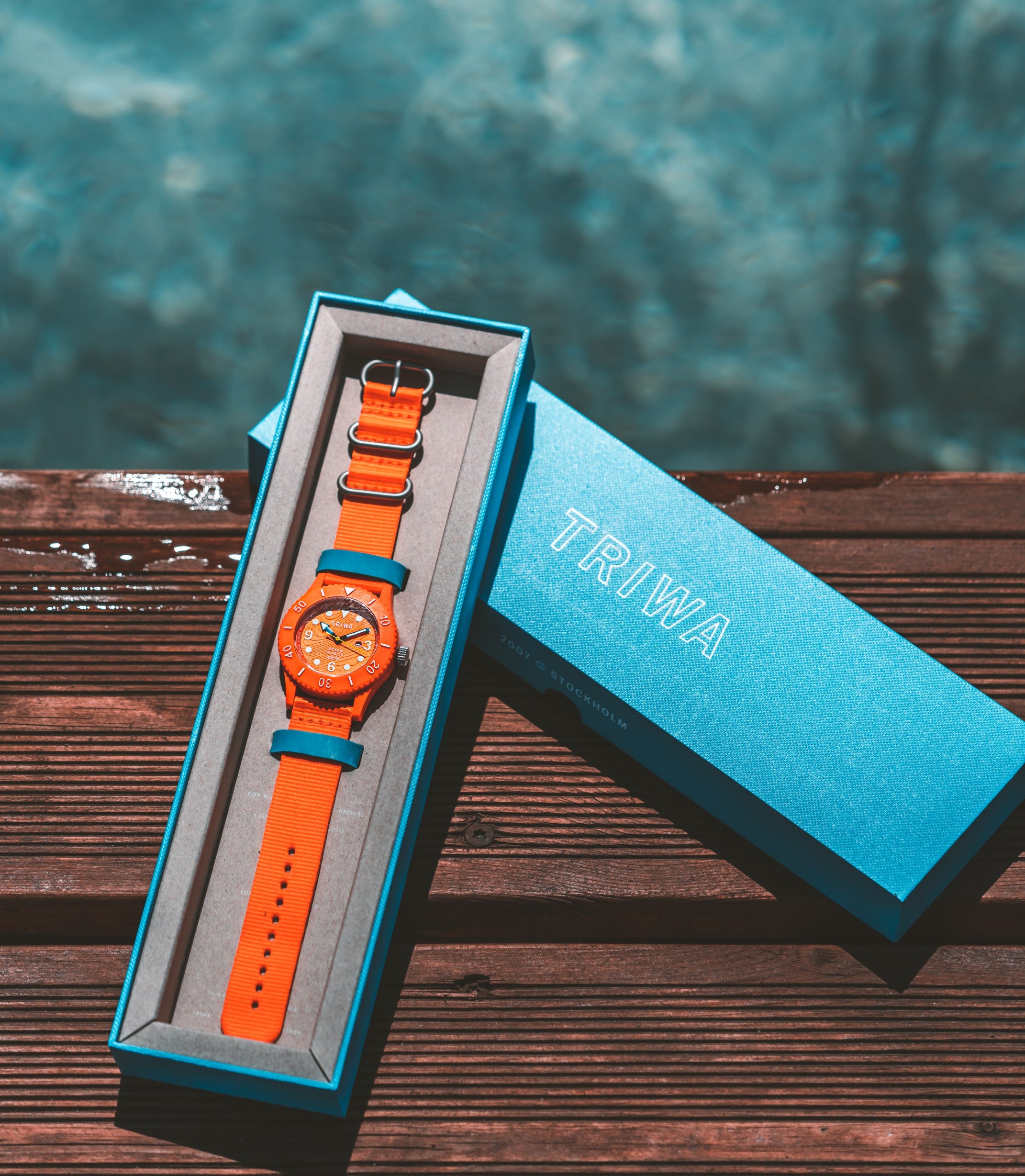 Orange watch with blue strap in a blue box on a wooden surface with a blurred natural background